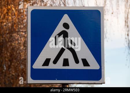 Traffic indicating sign, a blue crosswalk sign for pedestrians crossing the street or road on blur green trees and blue sky background in the city. No Stock Photo