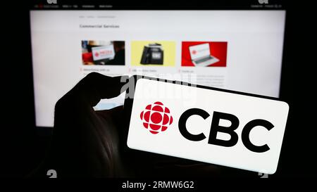 Personne détenant un téléphone cellulaire avec le logo de la Société radio-Canada (SRC) à l'écran devant la page Web. Concentrez-vous sur l'affichage du téléphone. Banque D'Images