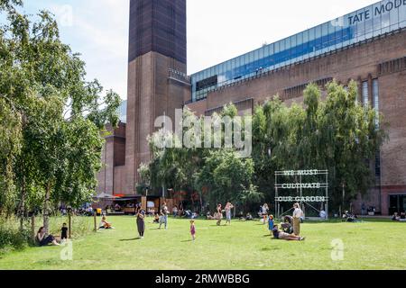 Les gens apprécient le soleil sur l'herbe devant la galerie d'art Tate Modern à Bankside, Londres, Royaume-Uni Banque D'Images