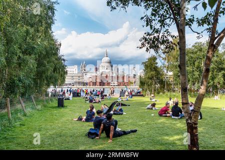 People enjoying the sun in a grassy area by the River Thames at Bankside, London, UK Stock Photo