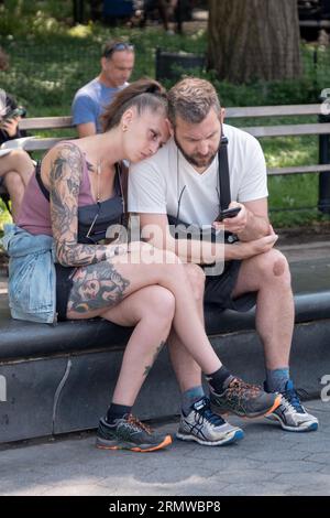 Un couple français fatigué fait une pause pour se reposer et vérifier un téléphone portable sur un banc dans Washington Square Park à Manhattan. Banque D'Images