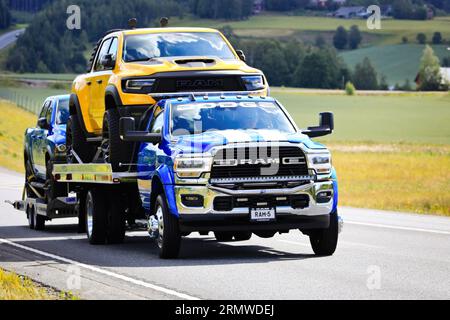 Puissant et personnalisé, le camion RAM 5500 transporte deux camionnettes, un RAM jaune et un 3e camion léger sur remorque. Autoroute 3, Finlande. 10 août 2023. Banque D'Images