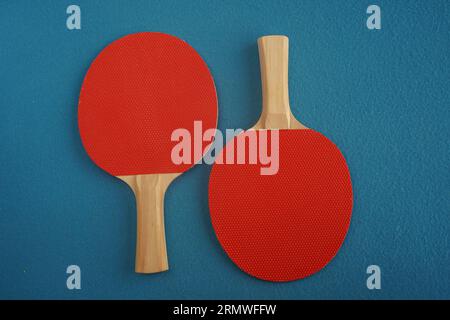 Deux raquettes rouges de tennis de table reposent à l'envers sur un fond bleu avec une vue rapprochée d'en haut. Jeu de loisirs. Équipement de sport. International Banque D'Images
