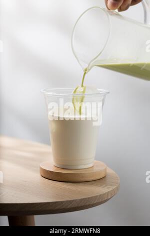 Verser du thé vert dans une tasse de lait. Banque D'Images