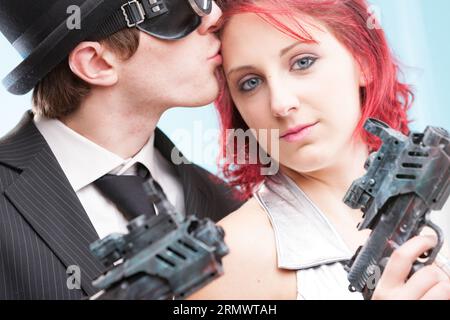 Deux mondes s'affrontent dans un baiser : l'espion super-héros portant un chapeau melon et sa superbe héroïne fantastique en argent. Avec des armes à rayons ultra-x en remorque, ils fi Banque D'Images
