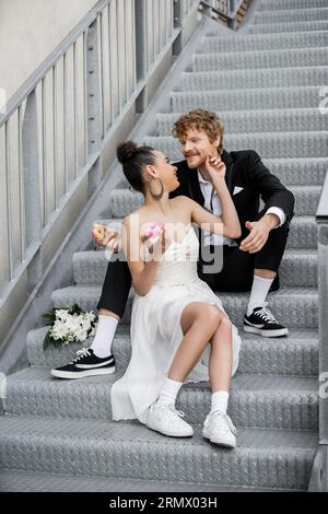 couple interracial avec beignets doux assis se regardant les uns les autres sur les escaliers de la ville Banque D'Images