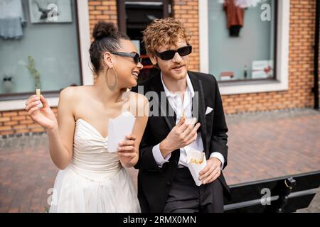 mariage en plein air, snacking, couple interracial élégant, tenue élégante, lunettes de soleil, frites Banque D'Images