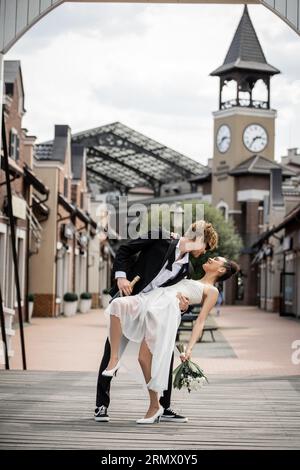 cérémonie de mariage dans la ville européenne moderne, jeune homme embrassant heureuse mariée afro-américaine dans la rue Banque D'Images