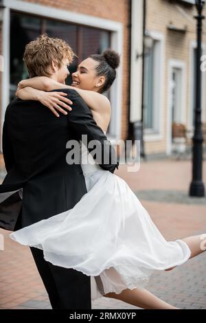 cérémonie de mariage en plein air, couple interracial ravi et élégant embrassant sur la rue de la ville Banque D'Images