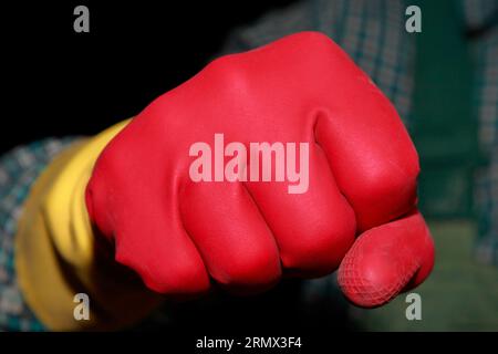 Le poing de l'homme dans les gants en caoutchouc rouge montre la force et la conduite. Sa poignée prête à maîtriser le travail de nettoyage à venir. Banque D'Images
