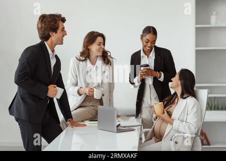 Heureuse femme enceinte latine bavardant avec ses collègues d'affaires multiraciaux tout en ayant une pause dans le bureau moderne Banque D'Images