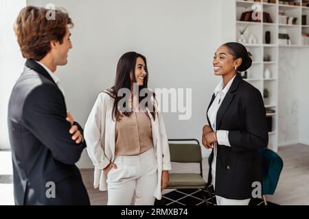 Sympathiques jeunes collègues multiraciaux employés de bureau debout dans la salle de conférence et bavardant pendant la pause Banque D'Images