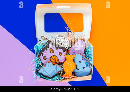 Biscuits de pain d'épice d'Halloween peints dans une boîte cadeau sur un fond géométrique lumineux. Banque D'Images