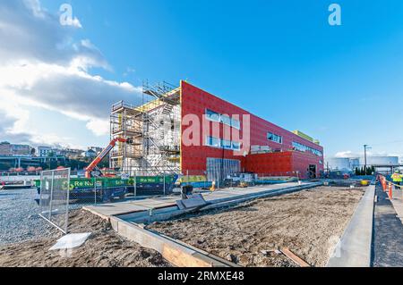 Un grand ascenseur de location orange avec son bras étendu au toit d'un bâtiment sur un chantier de construction. Il est utilisé pour transporter les matériaux de construction jusqu'au toit. Banque D'Images