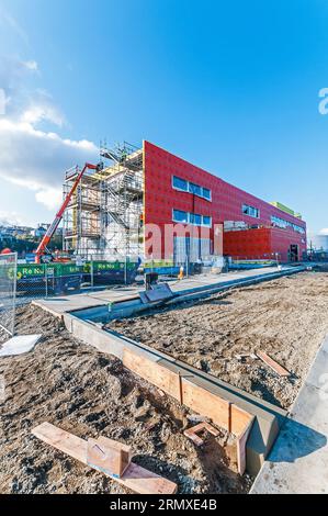 Un grand ascenseur de location orange avec son bras étendu au toit d'un bâtiment sur un chantier de construction. Il est utilisé pour transporter les matériaux de construction jusqu'au toit. Banque D'Images
