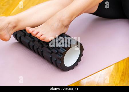 Using foam roller for self-massage of feet. Close up photo of fitness roller and female foot. Banque D'Images