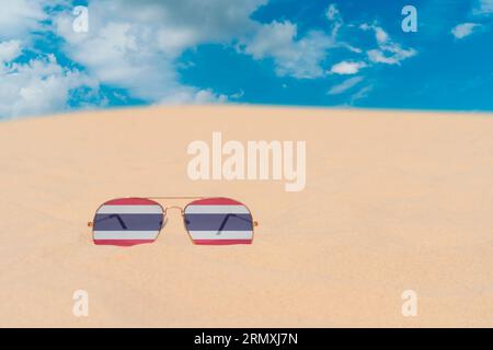 Lunettes de soleil avec des lunettes en forme de drapeau de la Thaïlande reposent sur le sable contre le ciel bleu. Concept de vacances d'été, voyage et tourisme en Thaïlande Banque D'Images