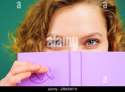 Portrait en gros plan de l'enseignante avec bloc-notes. Fournitures scolaires. Éducation, apprentissage. Retour à l'école. Étudiante se cachant derrière un livre ouvert Banque D'Images