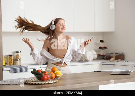 Heureuse jeune femme écoutant de la musique et dansant dans la cuisine moderne Banque D'Images