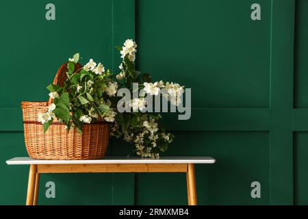 Panier en osier avec fleurs de jasmin sur la table de console près du mur vert Banque D'Images