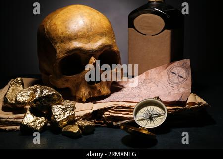 Crâne humain avec de vieux manuscrits, bouteille de rhum, pépites dorées et boussole sur fond noir Banque D'Images