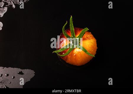 Wet yellow-red striped tomato on black wet background with water drops Stock Photo