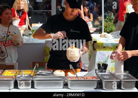 好椰 Oui le personnel de noix de coco cuillère des garnitures de mangue sur un dessert de pudding au lait de coco à Dragon Fes Food Festival Street Fair à New York, 27 août 2023. Banque D'Images