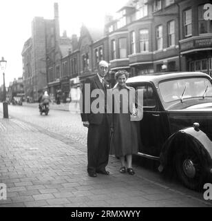 Années 1940, historique, un couple mûr bien habillé debout sur le trottoir par leur voiture de l'époque, Angleterre, Royaume-Uni. Banque D'Images