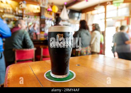 Vue générale d'une pinte complète de Guinness Irish Dry stout Beer dans un pub animé coloré dans la ville de Cobh, Irlande. Banque D'Images