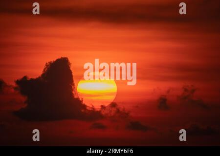 Early morning sunrise with big bowl of sun visible rising through clouds and mist on caribbean coast at Limon province in Costa Rica Stock Photo