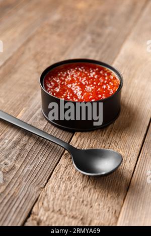 Caviar de saumon rouge dans une boîte de conserve noire ouverte et une cuillère noire sur fond de bois. Fruits de mer délicats utiles, poisson en conserve. Banque D'Images