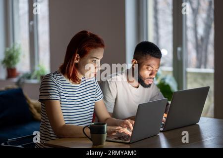 Les entrepreneurs ciblés femme caucasienne homme afro-américain travaillent sur des ordinateurs portables dans le bureau à domicile ensemble. Banque D'Images