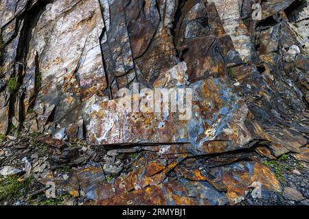 Des couches pliées d'ardoise en gris, brun rouille et orange forment une paroi rocheuse près du village de Chesho à Tusheti, dans la municipalité d'Akhmeta, région de Kakheti, Géorgie. De grandes dalles se sont détachées et gisent inclinées les unes sur les autres. Devant, des fragments et des éclats recouvrent le sol. De l'herbe et de la mousse poussent dans les fissures. Les maisons et les tours défensives des villages tushetiens sont construites en dalles d'ardoise empilées à sec. Les Tushetiens semi-nomades vivent dans les villages de montagne uniquement de juillet à septembre. Ils passent le reste de l'année dans la vallée plus basse d'Alvani. Banque D'Images