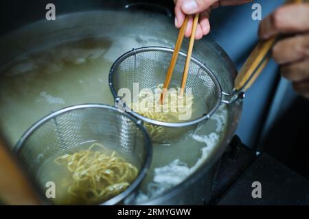 D'en haut de la culture anonyme personne cuisinant des nouilles dans l'eau avec des baguettes pour ramen savoureux Banque D'Images