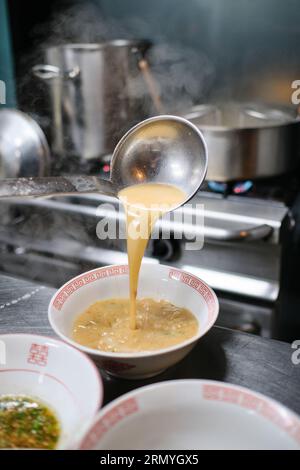 Bouillon étant versé dans le bol de la louche en métal en cours de cuisson traditionnelle soupe ramen dans la cuisine Banque D'Images