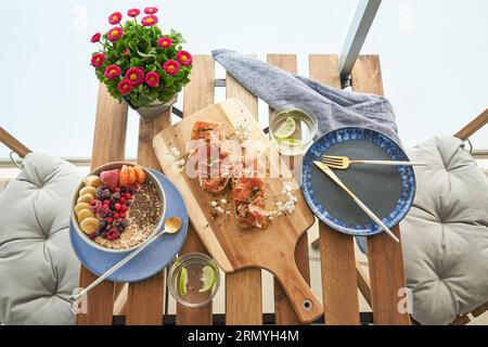 Vue de dessus de délicieux toasts avec prosciutto servi sur une planche à découper près d'un bol de flocons d'avoine sains avec des baies assorties et des verres d'eau de citron vert placés sur t Banque D'Images