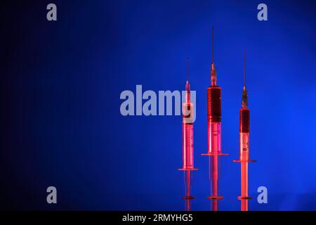 Gros plan de seringues médicales avec aiguilles remplies de vaccin COVID19 et placées sur une surface réfléchissante en néon Banque D'Images