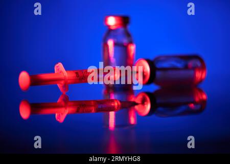 Gros plan de flacons médicaux et de seringues remplis de vaccin COVID19 et préparés pour la vaccination en néon Banque D'Images
