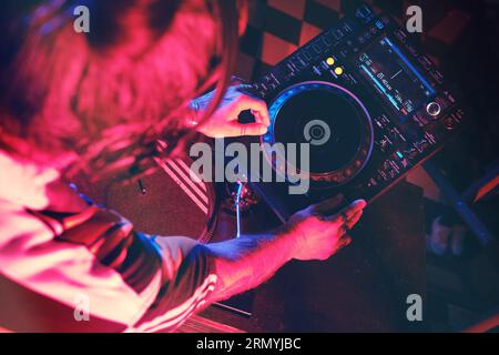 D'en haut de la récolte anonyme DJ talentueux jouant la chanson sur le lecteur CDJ moderne tout en travaillant dans la boîte de nuit avec éclairage faible Banque D'Images