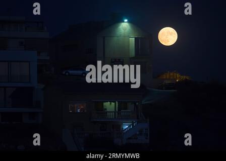 La superlune bleue, la deuxième superlune d'août, se lève sur le ciel à côté des bâtiments de la plage de 'la Araña'. La superlune bleue se déroule comme l'un des événements astronomiques les plus frappants du mois. Lorsque la pleine lune a lieu, elle apparaît plus grande et plus lumineuse que la normale. Banque D'Images