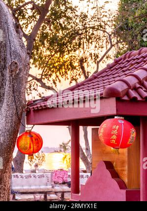 Sun shining through red chinese style lanterns,peaceful scene in temple grounds,next to the Mekong river in the south of Laos. Stock Photo