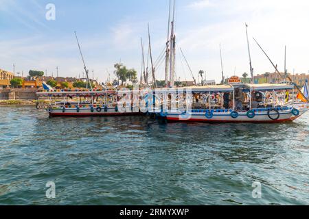 Bateaux de croisière fluviale touristique colorée et felouques sur le Nil africain alors qu'ils voyagent à travers le quartier central de Louxor, en Égypte. Banque D'Images