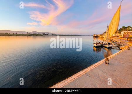 Feluccas, bateaux à voile traditionnels en bois, sont amarrés le long de la rive du Nil, à Louxor, en Égypte au coucher du soleil. Banque D'Images