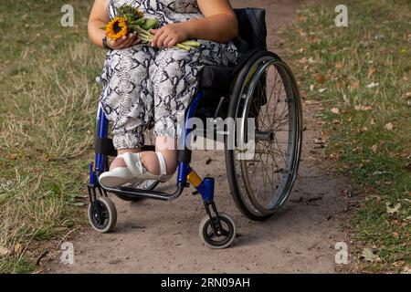 Cropped Jeune femme avec petite stature sur fauteuil roulant tient bouquet de fleurs dans Green Park au jour d'été. Femme adulte handicapée. Relation Banque D'Images