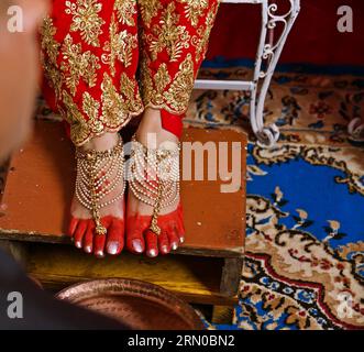 Cérémonie de mariage coutumier népalais les pieds de la mariée ornés de motifs complexes de henné et ornés de ongles d'orteil avec sarée rouge et tapis bleu. Banque D'Images