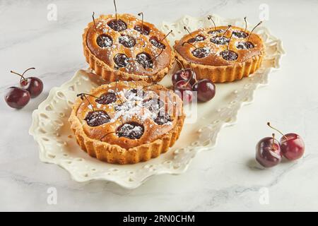 French Flair, Cherry Clafoutis présenté sur White Marble. Tentation alléchante : clafoutis et cerises sur marbre. Banque D'Images