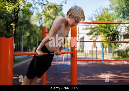 Athletic boy stretched upward and holding onto the tourniquet with his hands. Street workout on a horizontal bar in the school park. Stock Photo