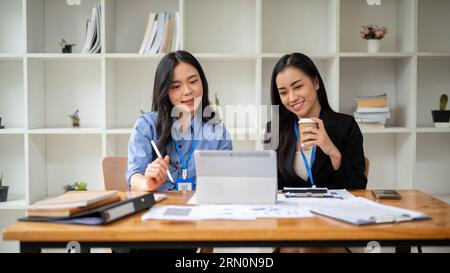 Deux comptables ou femmes d'affaires asiatiques professionnelles et heureuses se concentrent sur un projet, regardant l'écran de tablette, brainstorming et analysant Banque D'Images