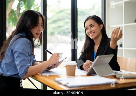 Two attractive and professional Asian businesswomen or accountants are discussing work and planning a financial project at a table in the office toget Banque D'Images