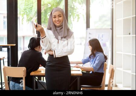 Une femme d'affaires musulmane asiatique attrayante et confiante ou une dirigeante portant un hijab sourit à la caméra tout en se tenant debout dans la salle de réunion. Banque D'Images